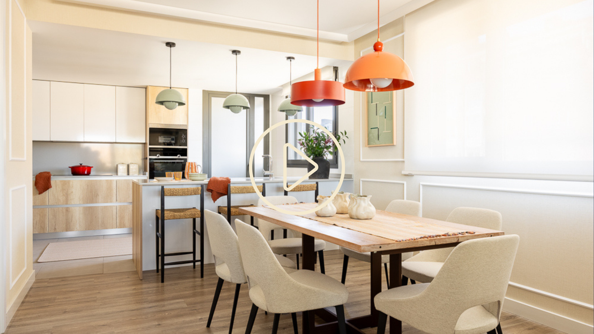 Imagen previa de un vídeo de María del Valle Interiorismo con comedor y cocina integrada, lámparas colgantes en tonos rojos y verdes, mesa de madera y sillas tapizadas en beige.
