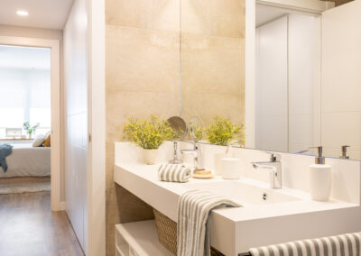 Baño con lavabo doble en blanco, espejo de gran formato y revestimiento en tonos piedra.