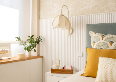 Dormitorio con cama doble, cabecero azul, cojines decorativos en tonos mostaza y verde, y papel pintado vegetal.
