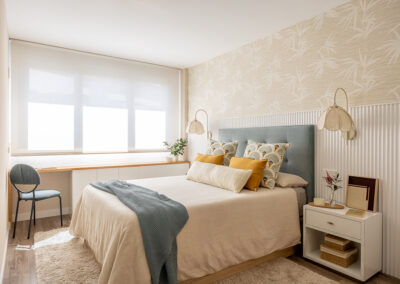 Dormitorio principal con cama doble, cabecero azul, mesillas blancas y zona de trabajo junto a la ventana.