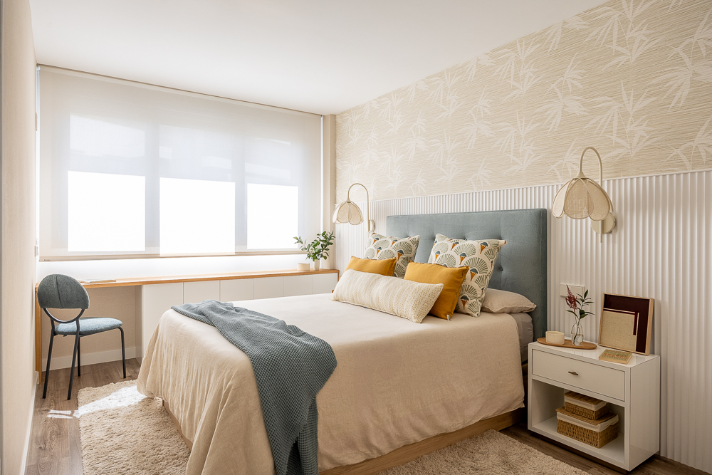 María_del_Valle_Interiorismo_dormitorio_matrimonio_cama_cojines_cabecero_molduras_papel_pintado_hojas Dormitorio principal con cama doble, cabecero azul, mesillas blancas y zona de trabajo junto a la ventana.