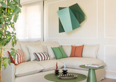 Salón diseñado por María del Valle Interiorismo con sofá en tonos neutros, mesas auxiliares verdes y escultura de pared geométrica en verde.