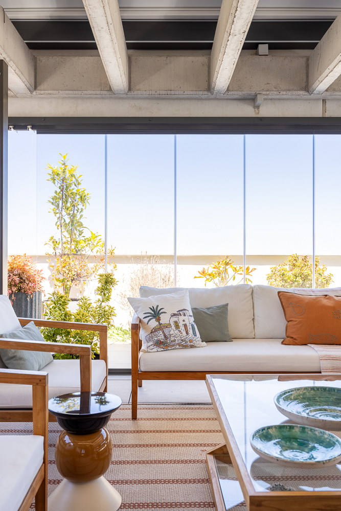 Terraza de ático diseñada por María del Valle Interiorismo con sofás de madera, cojines decorativos y mesa auxiliar.