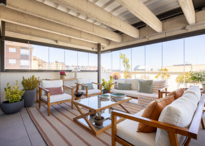 Terraza acristalada con sofás y cojines decorativos en tonos cálidos y verdes.