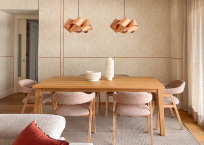 Comedor con mesa de madera, alfombra neutra y pared con papel pintado y molduras decorativas.