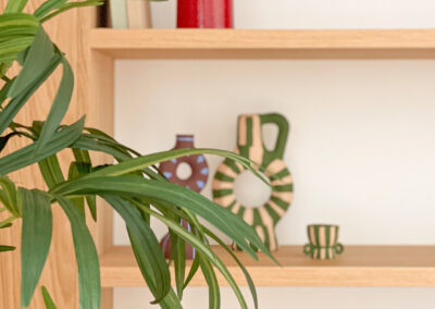 Detalle de estantería con planta y jarrones decorativos sobre baldas de madera.