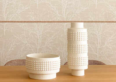 Jarrones de cerámica blanca sobre mesa de madera con pared decorada con papel pintado.