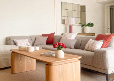 Sofá modular en tonos neutros con cojines rojos y mesa de centro rectangular en madera clara.