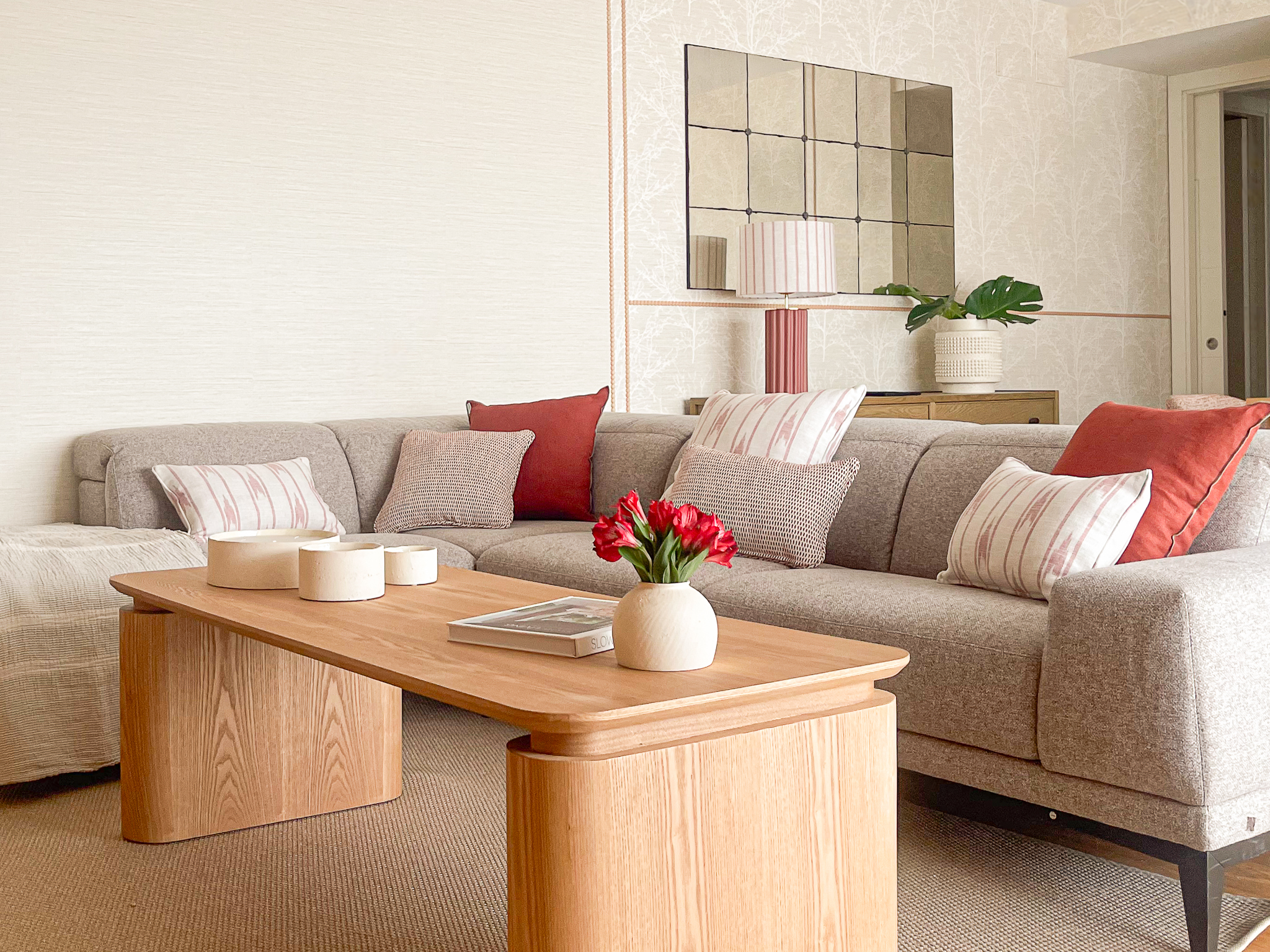 Sofá modular en tonos neutros con cojines rojos y mesa de centro rectangular en madera clara.