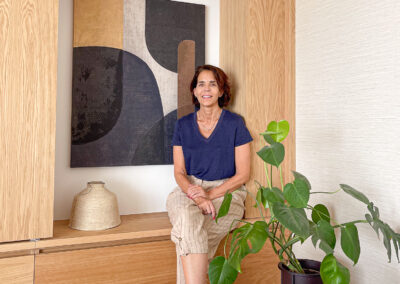 Maria del Valle en salón junto a mueble de roble con cuadro abstracto.