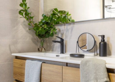 Baño con mueble suspendido de madera, encimera blanca, grifería negra y revestimientos en tonos neutros.