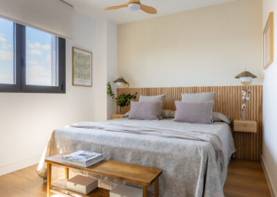 Dormitorio principal con cabecero de madera de lamas, mesillas suspendidas, textiles en tonos neutros y decoración minimalista.
