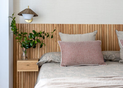 Detalle de dormitorio con cabecero de madera de lamas, mesilla suspendida, textiles en tonos neutros y decoración natural.