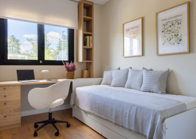 Despacho en casa con escritorio a medida, cama individual integrada, estantería vertical y decoración en tonos neutros.