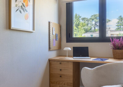 Escritorio a medida en madera junto a ventana, con cajonera, silla tapizada y decoración en tonos neutros.