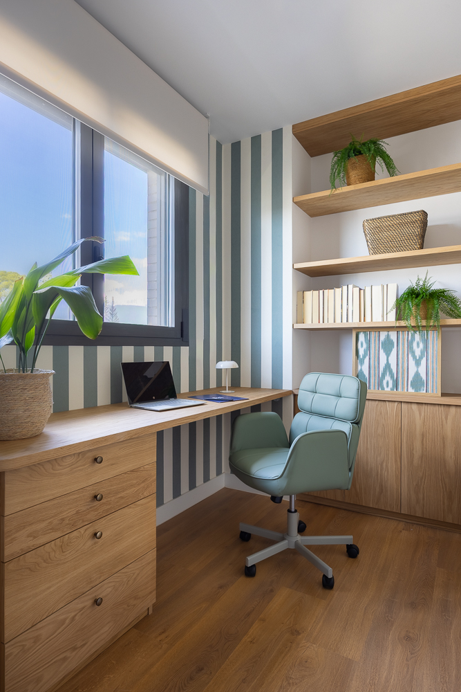 Zona de estudio con escritorio de madera a medida, silla verde, estanterías abiertas y papel pintado a rayas verticales en tonos suaves.